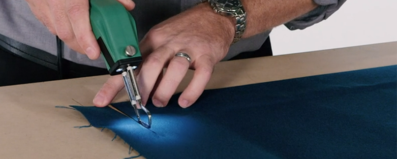 Masculine hands demonstrating a professional hotknife cutting blue fabric