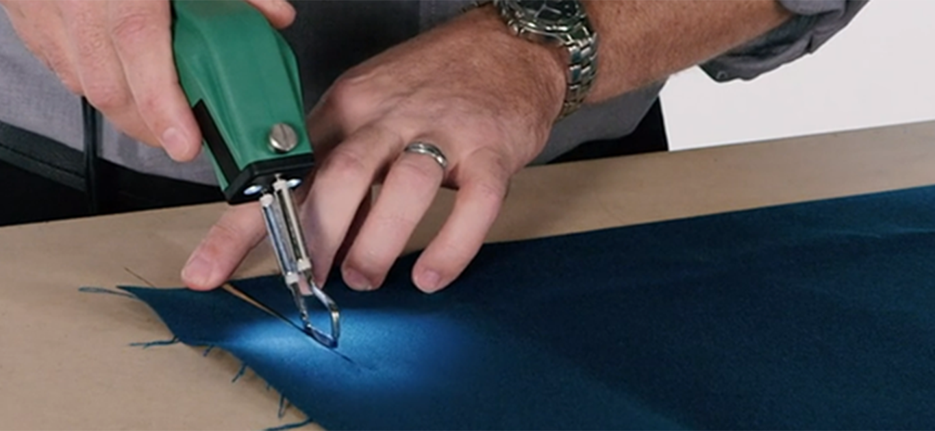 masculine hands demonstrating a professional hotknife cutting blue fabric