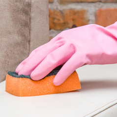main collée en caoutchouc rose à l'aide d'une éponge orange pour nettoyer le tissu d'ameublement beige