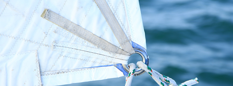 Boat sail and sail hardware reinforced with non-adhesive marine-grade performance fabric tape.