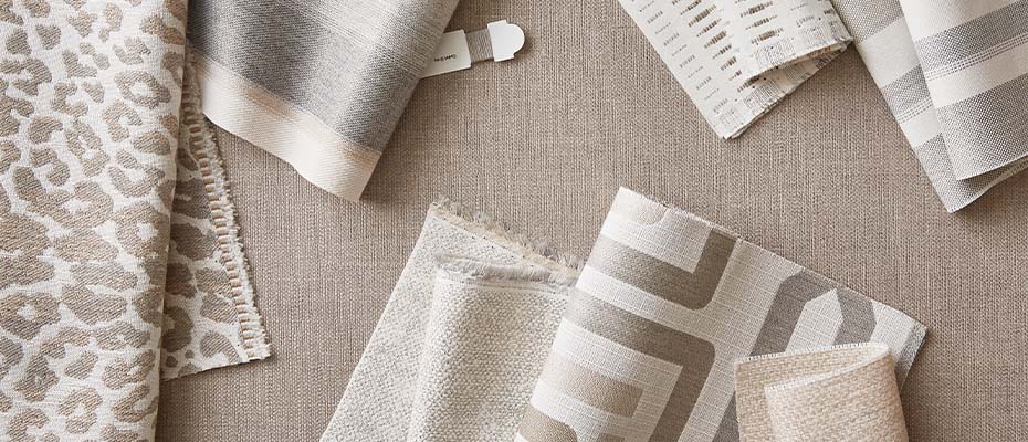 7 beige and grey patterned fabric displays and one spool of thread on larger fabric background